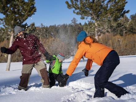 A family of three play in the snow during winter in Big Bear Lake.